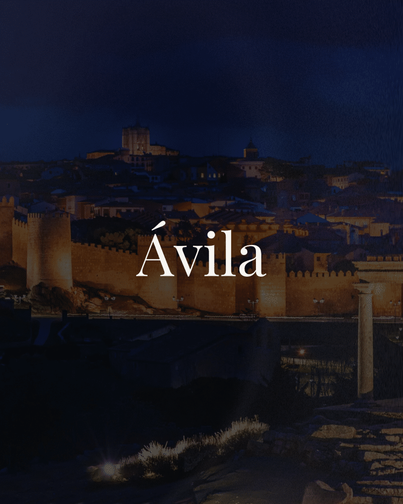 Vista nocturna de la ciudad de Ávila, destacando sus murallas iluminadas y el paisaje urbano.