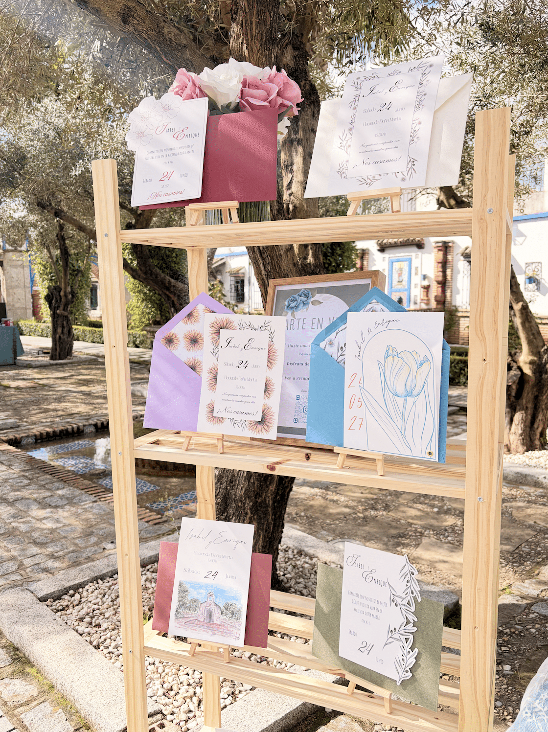 Muestra de papelería de boda en un soporte de madera, con invitaciones coloridas y diseños artísticos.