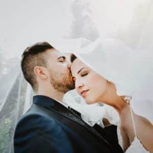 Pareja de novios compartiendo un tierno beso, con la novia luciendo un velo y el novio un traje elegante.