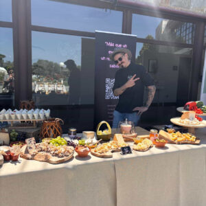 Mesa de quesos y embutidos decorada con frutas, acompañada de un catering profesional en un evento.