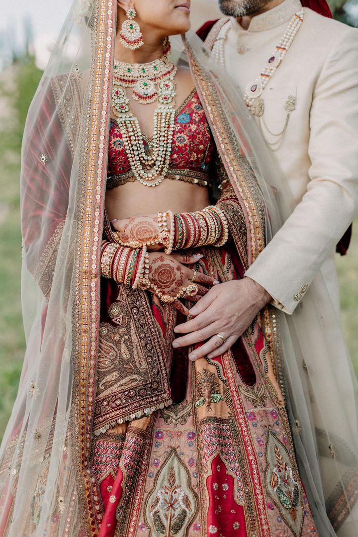 Pareja vestida con trajes tradicionales, ella lleva un sari colorido y él un atuendo claro, en un entorno natural.
