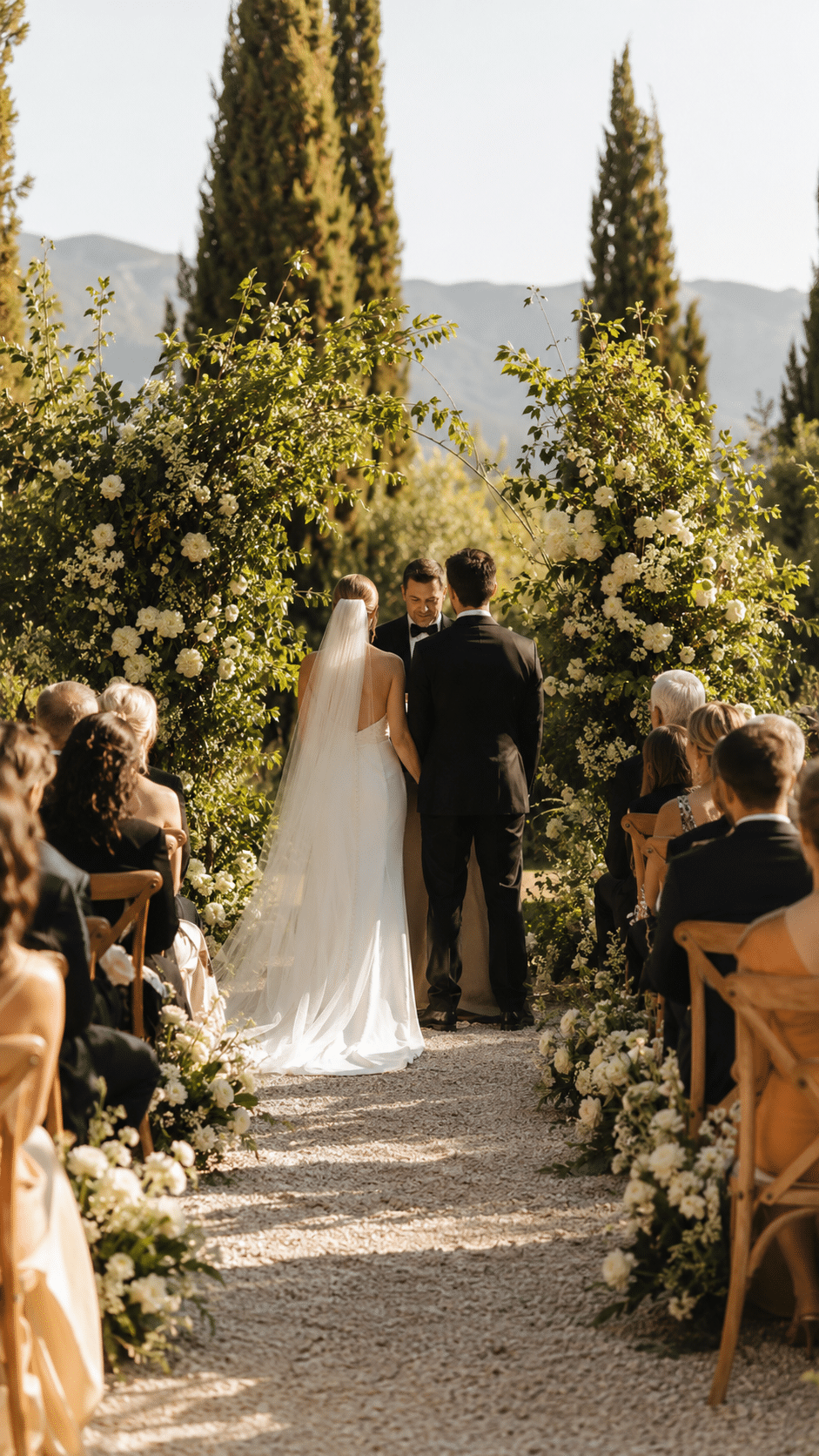 Pareja en ceremonia de boda al aire libre, rodeada de flores y con invitados sentados en sillas de madera.