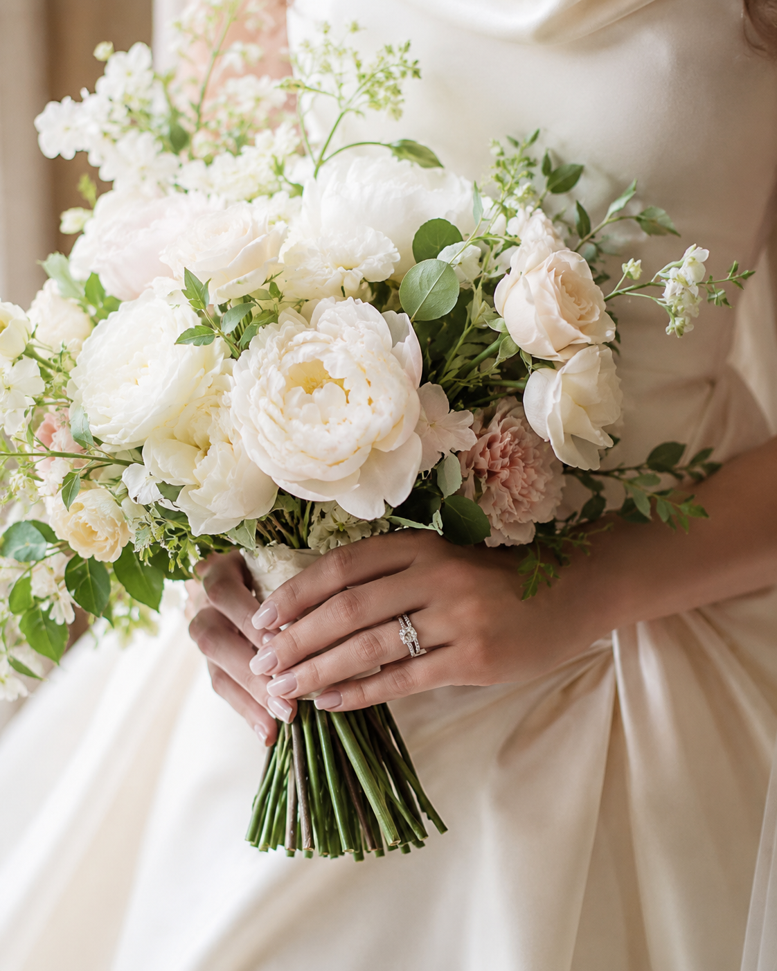 31031a92-bf01-4cfa-bd60-606cb8f71fb6 Ramo de novia con flores blancas y rosas, sostenido por manos que llevan un anillo de compromiso.