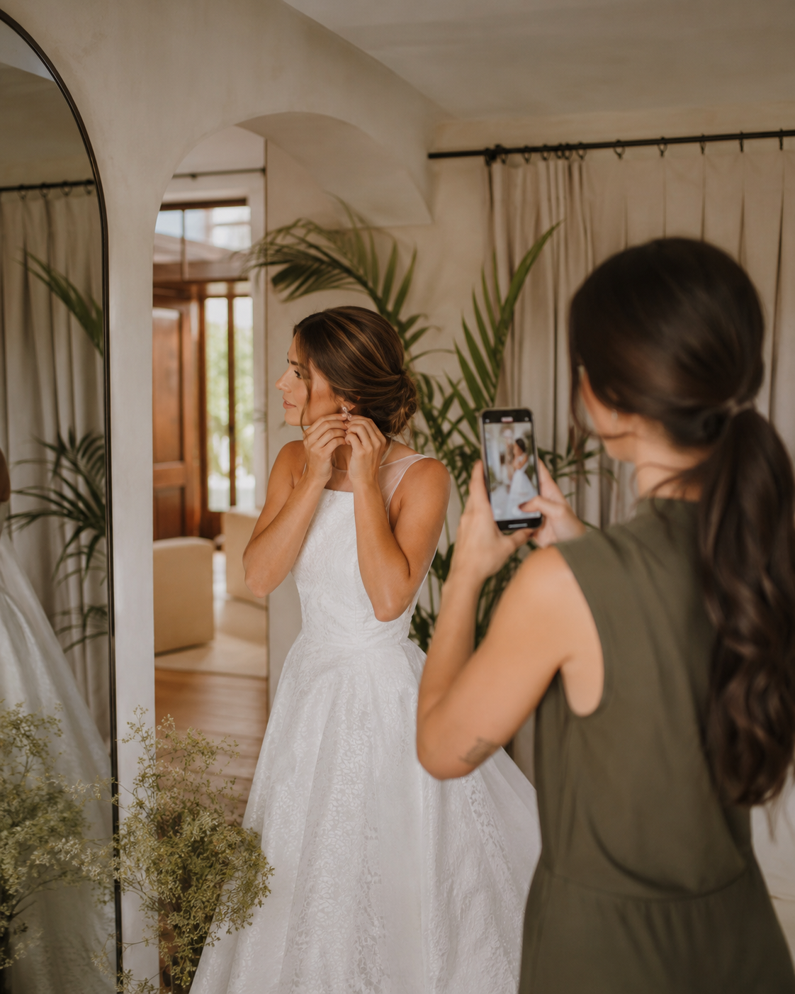 3f0278dd-fe28-47bd-8372-f60fc434346e Novia ajustándose los pendientes frente al espejo mientras una amiga la fotografía. Decoración minimalista de fondo.