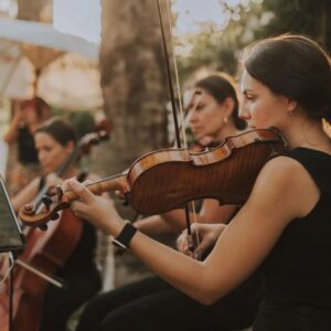 Músicos tocando instrumentos de cuerda en un ambiente al aire libre, creando una atmósfera romántica.