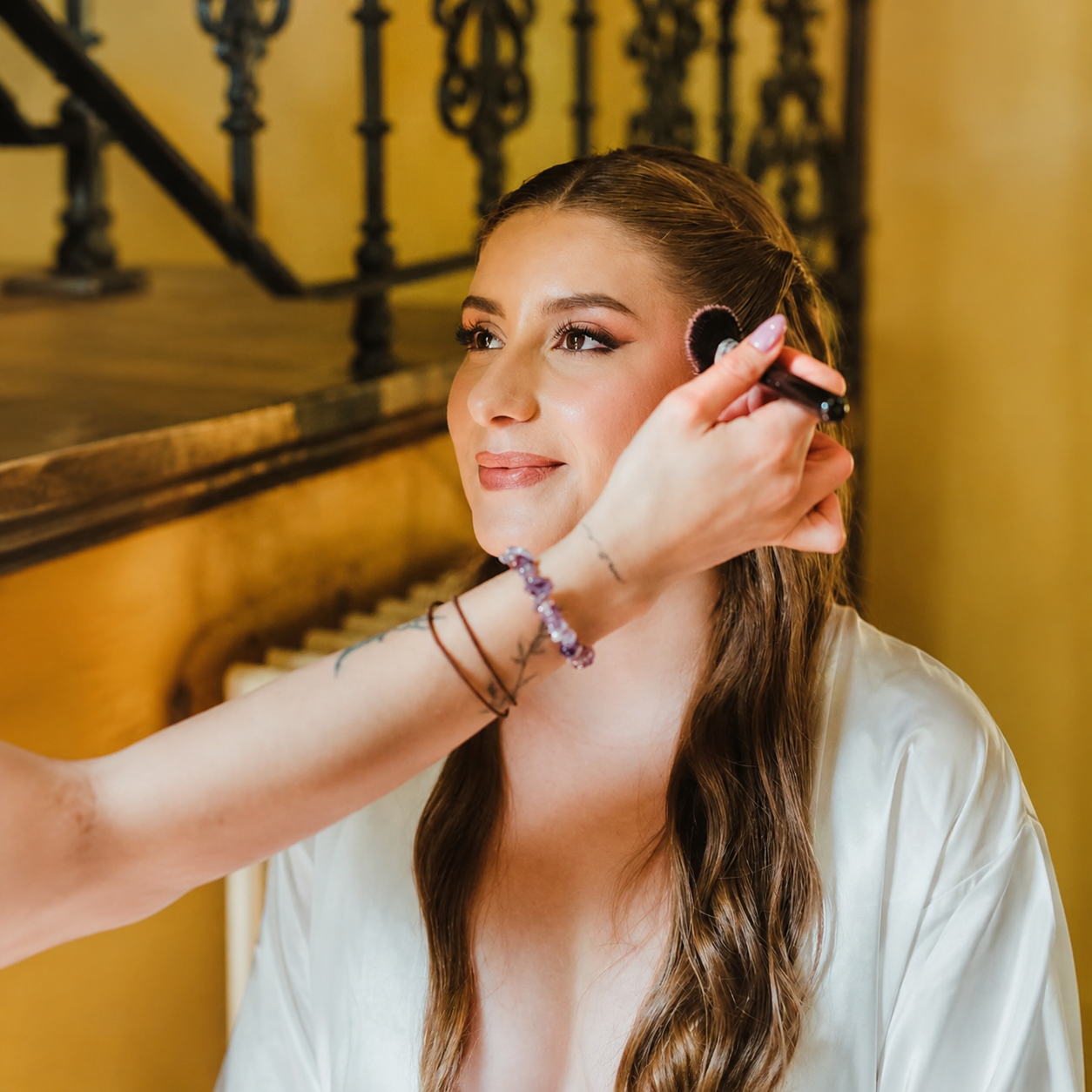 6cb47834-9f9c-444d-8055-aa77032e9ed7 Mujer recibiendo maquillaje profesional en un ambiente cálido y elegante.