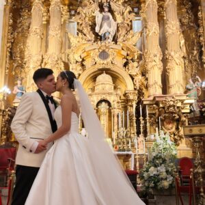 Pareja de novios besándose frente a un altar dorado y decorado en una iglesia.
