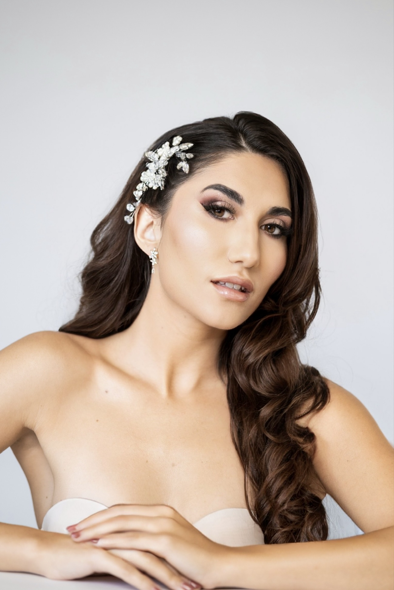 Image Mujer con maquillaje elegante y peinado con ondas y adorno floral blanco en el cabello.
