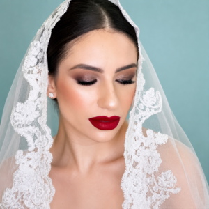 Novia con velo de encaje y maquillaje elegante con labios rojos y ojos ahumados.