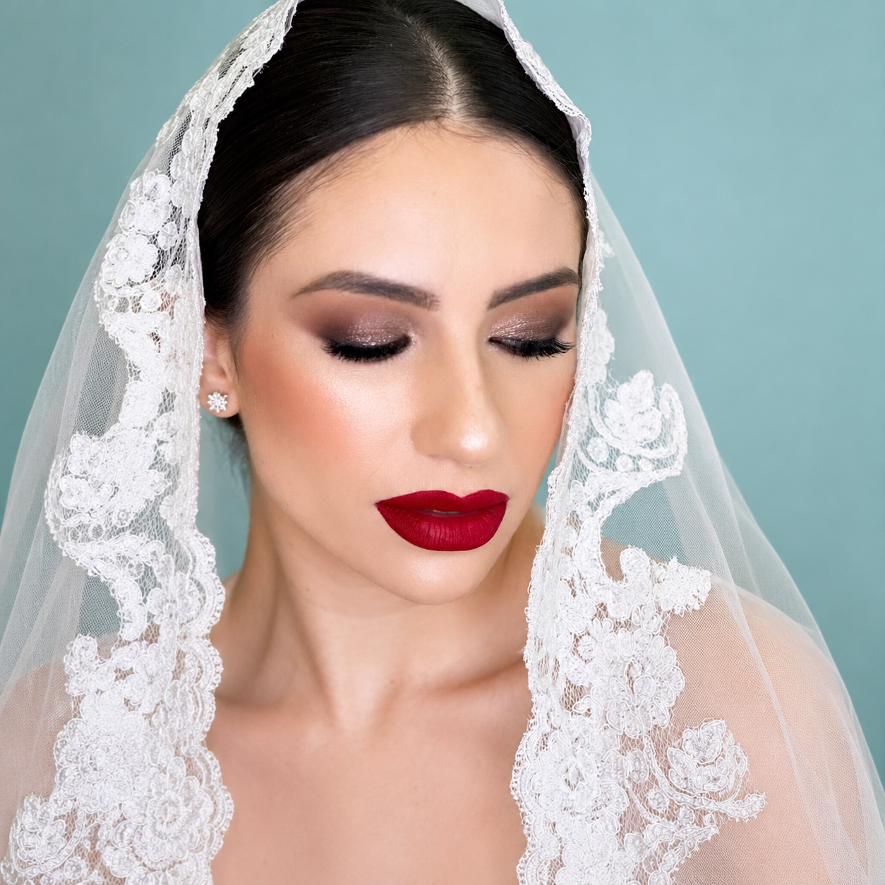 c5ebfd23-69a3-408f-8c96-3c6f16b7a600 Novia con velo de encaje y maquillaje elegante con labios rojos y ojos ahumados.