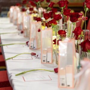 Mesa larga con manteles blancos, rosas rojas en jarrones y cajas de regalo alineadas.