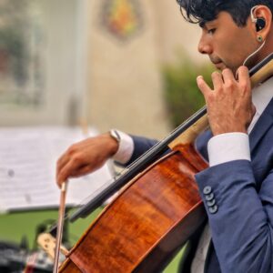 Hombre tocando violonchelo con partitura al fondo en un entorno interior.