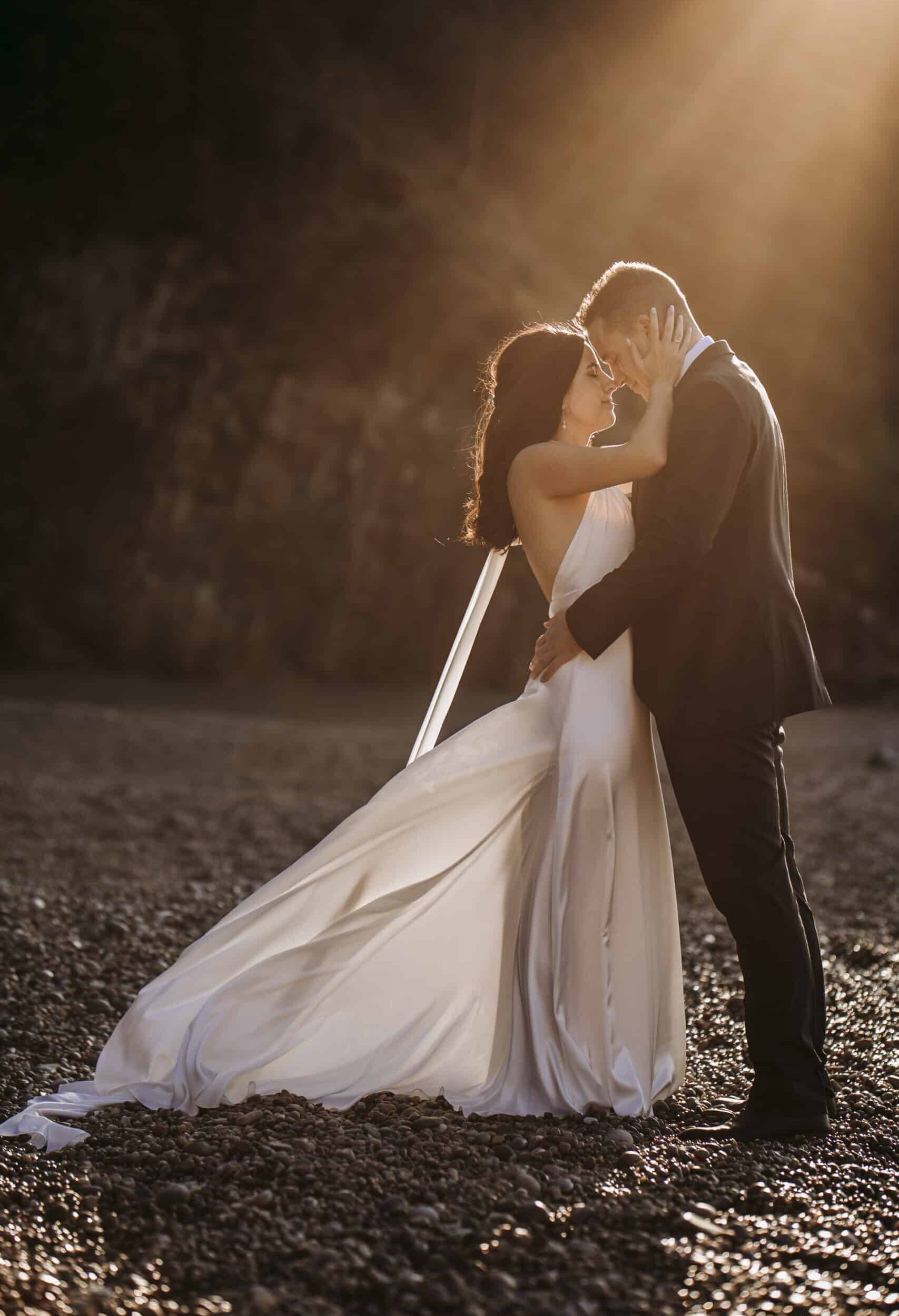 BODA FERNANDO Y SANDRA - 1093 Pareja de novios abrazados bajo luz cálida en un entorno natural con suelo rocoso.