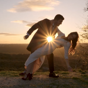 Pareja bailando al atardecer en un paisaje natural con árboles y cielo despejado.