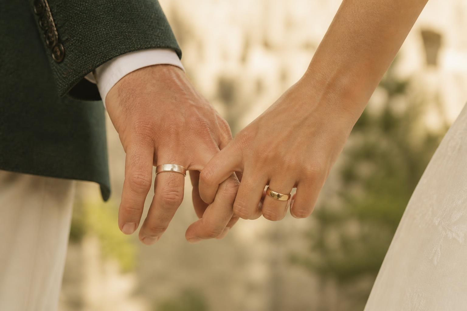 Manos entrelazadas de una pareja mostrando alianzas de oro amarillo y oro blanco