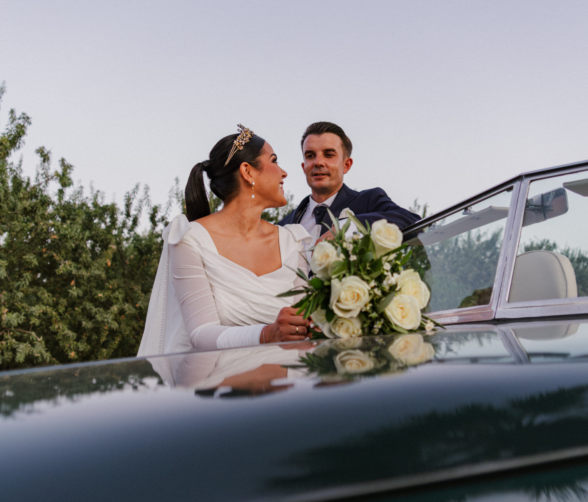 20-06-517 Pareja de novios sonrientes en un coche descapotable con ramo de flores blancas.