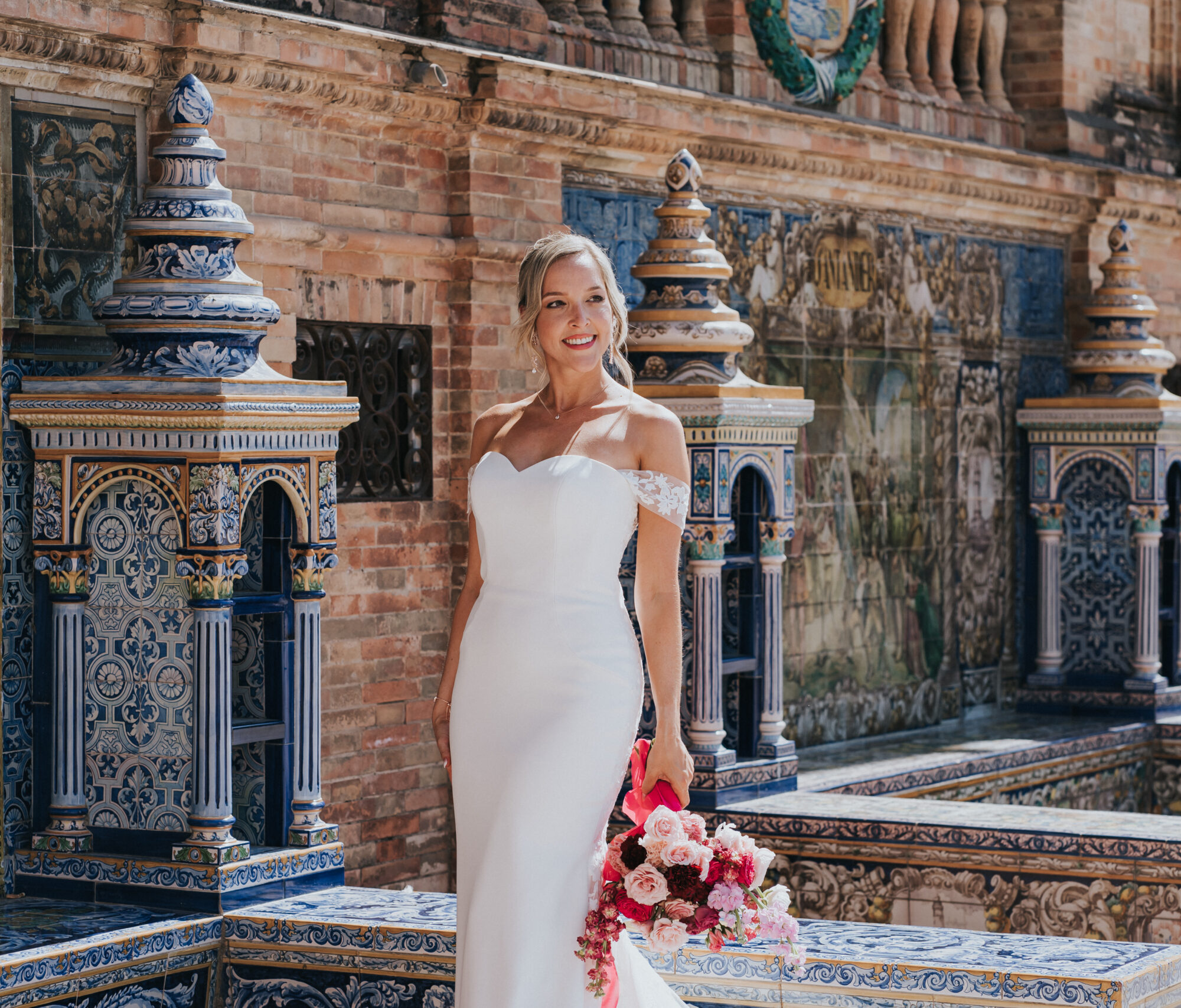 Boda David y Harley SEYMA -Fotografía-368 Mujer con vestido blanco y ramo de flores rosas posa junto a muro decorado con azulejos coloridos.