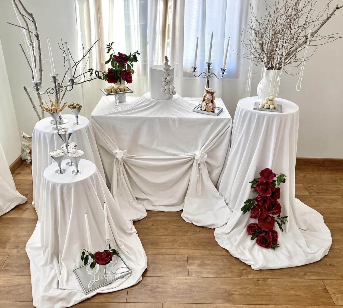 image00001 Mesa y pedestales con telas blancas, decorados con rosas rojas y ramas secas en jarrones blancos.