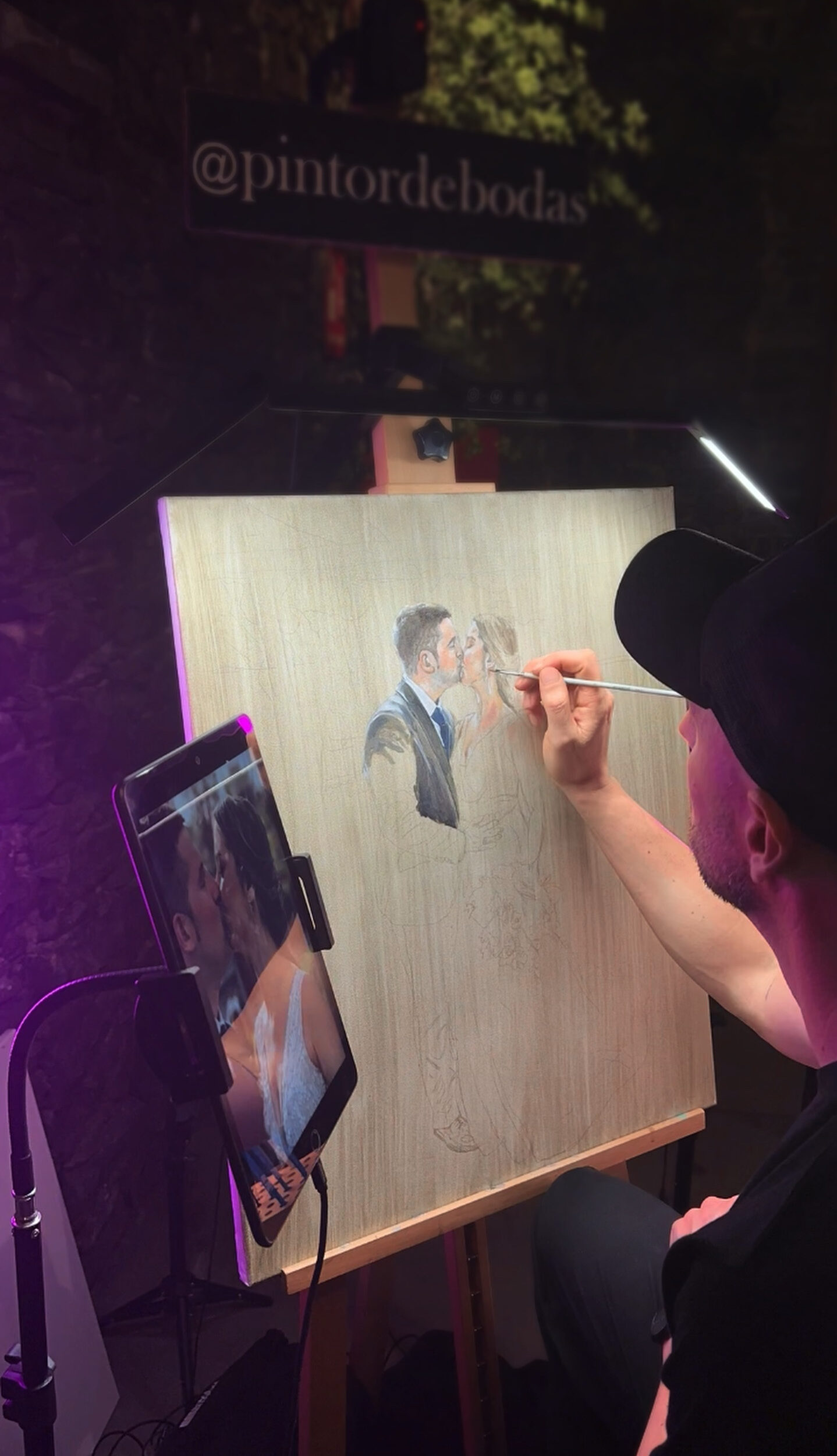 Pintando en Vivo 16 Artista pintando un retrato en un caballete iluminado durante un evento nocturno.