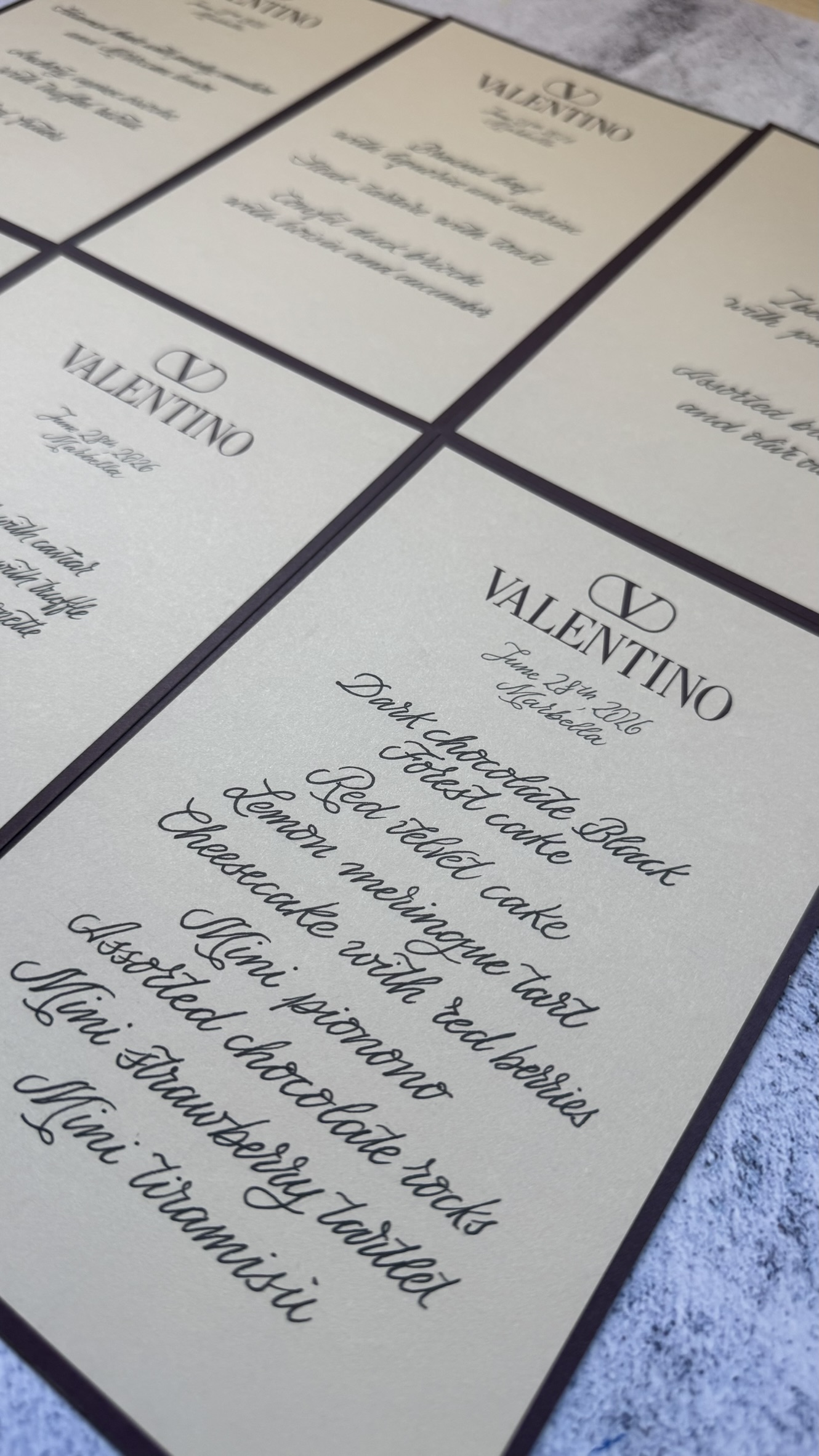menus-boda-benditacaligrafia Tarjetas con menús impresos en papel crema con texto en caligrafía negra sobre fondo gris.